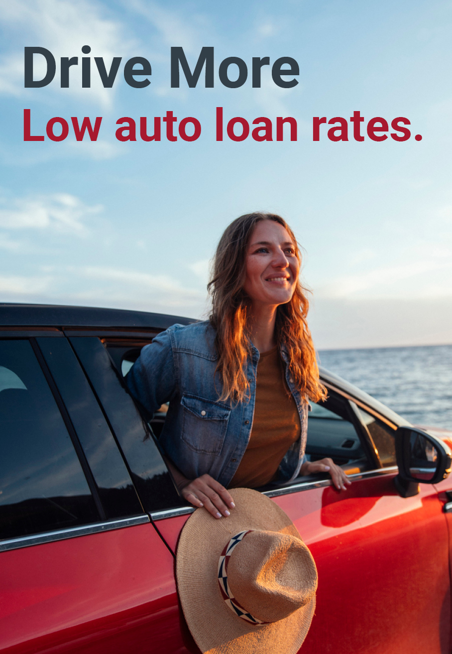 A woman leans out of the car window upon arriving at the beach. Text on image reads: Drive More. Low auto loan rates.