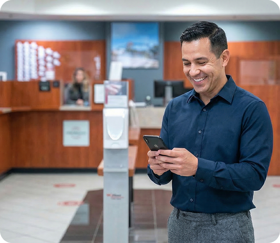 A man smiling while using his phone in the lobby of a bank