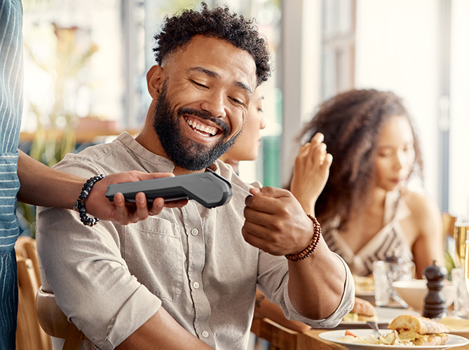 A man smiling while swiping a credit card at a restaurant