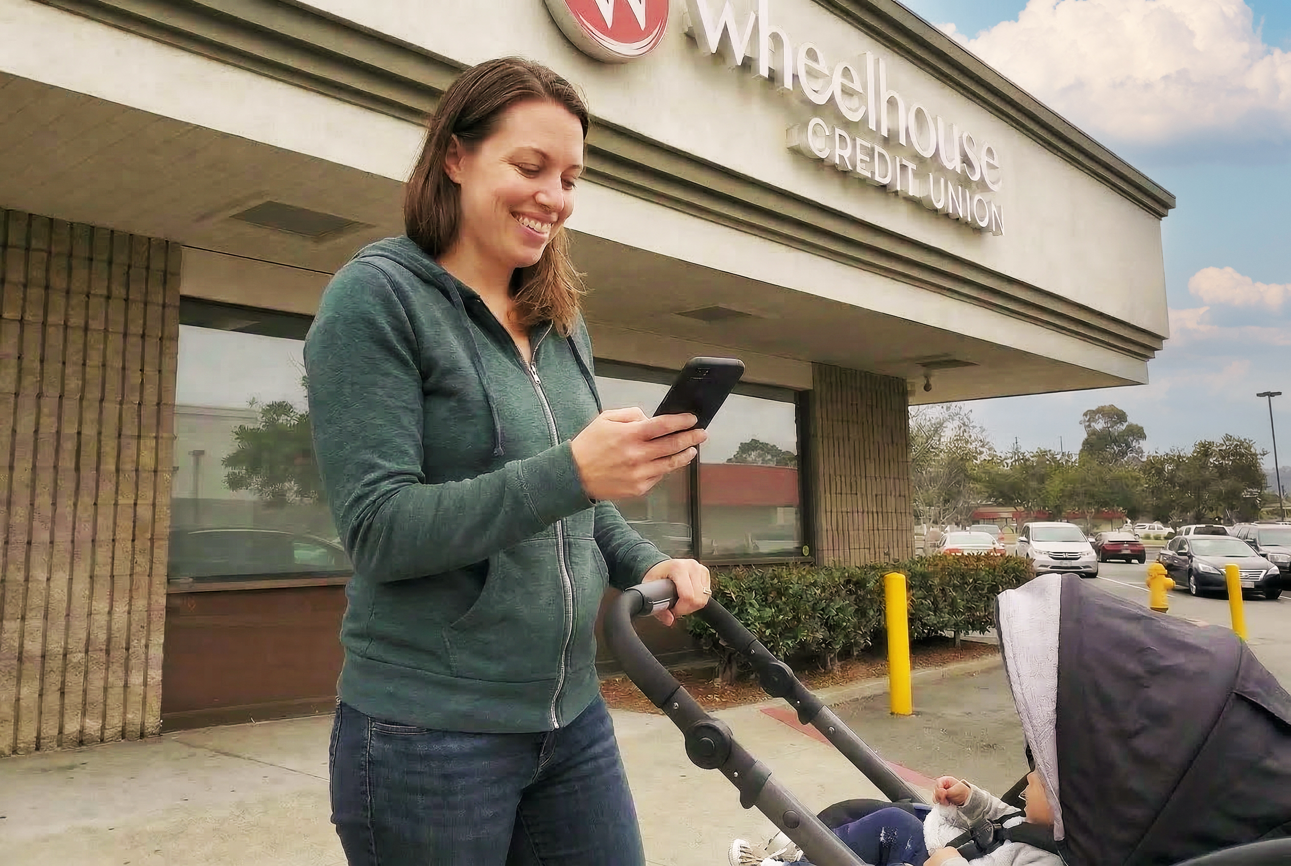 A woman pushing a stroller and looking at her smartphone outside of the Wheelhouse El Cajon branch