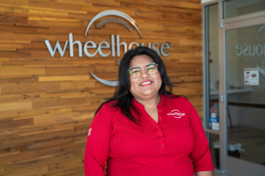 A woman in a Wheelhouse shirt smiling and standing in front of a Wheelhouse branch