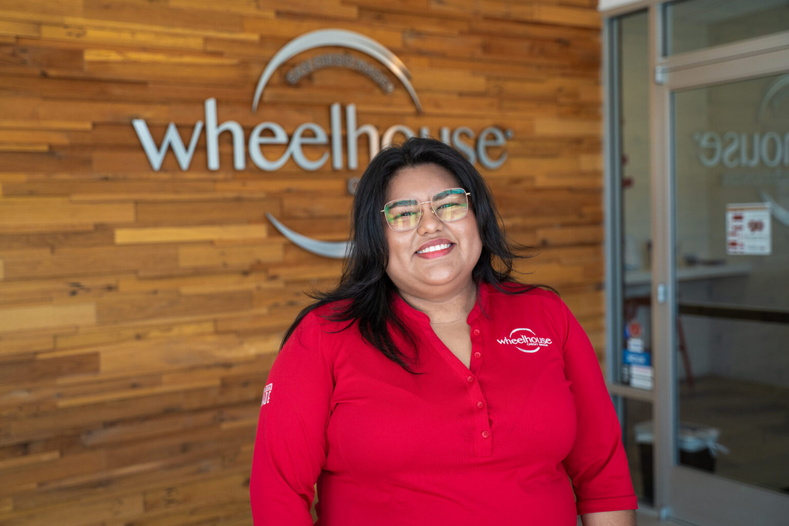 A woman in a Wheelhouse shirt smiling and standing in front of a Wheelhouse branch