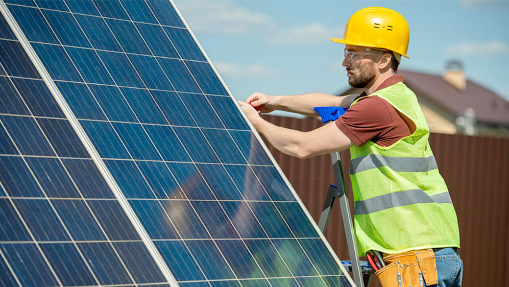 A man in a hard hat and safety vest installing a solar panel