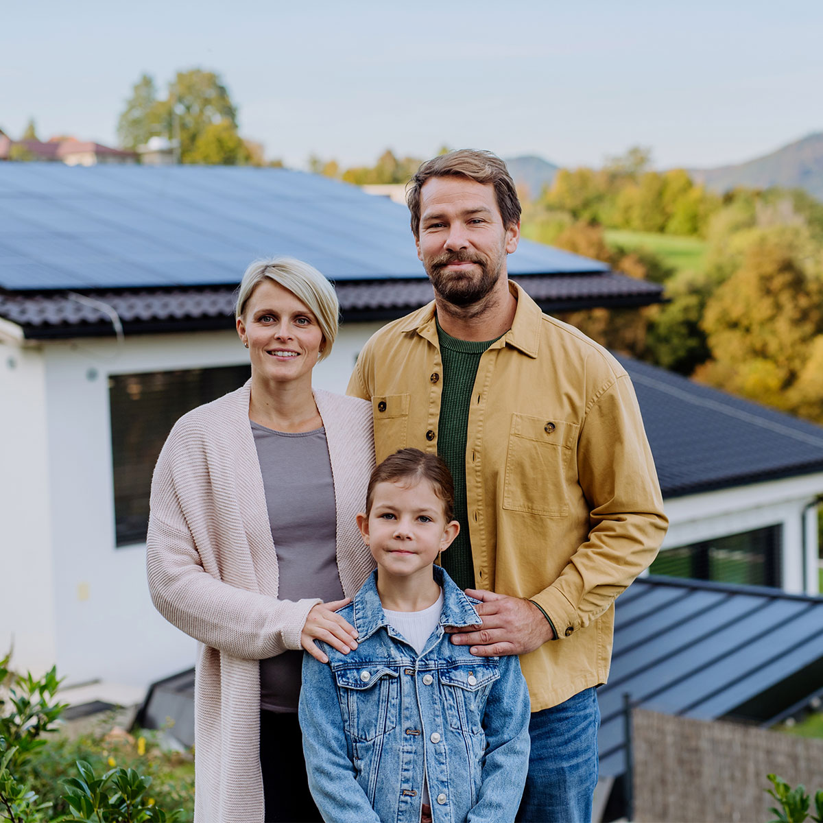 A family standing in front of their home with solar panels on the roof