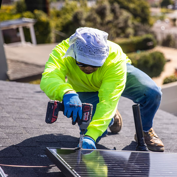 A man in a neon shirt installing a Solar Panel on a roof