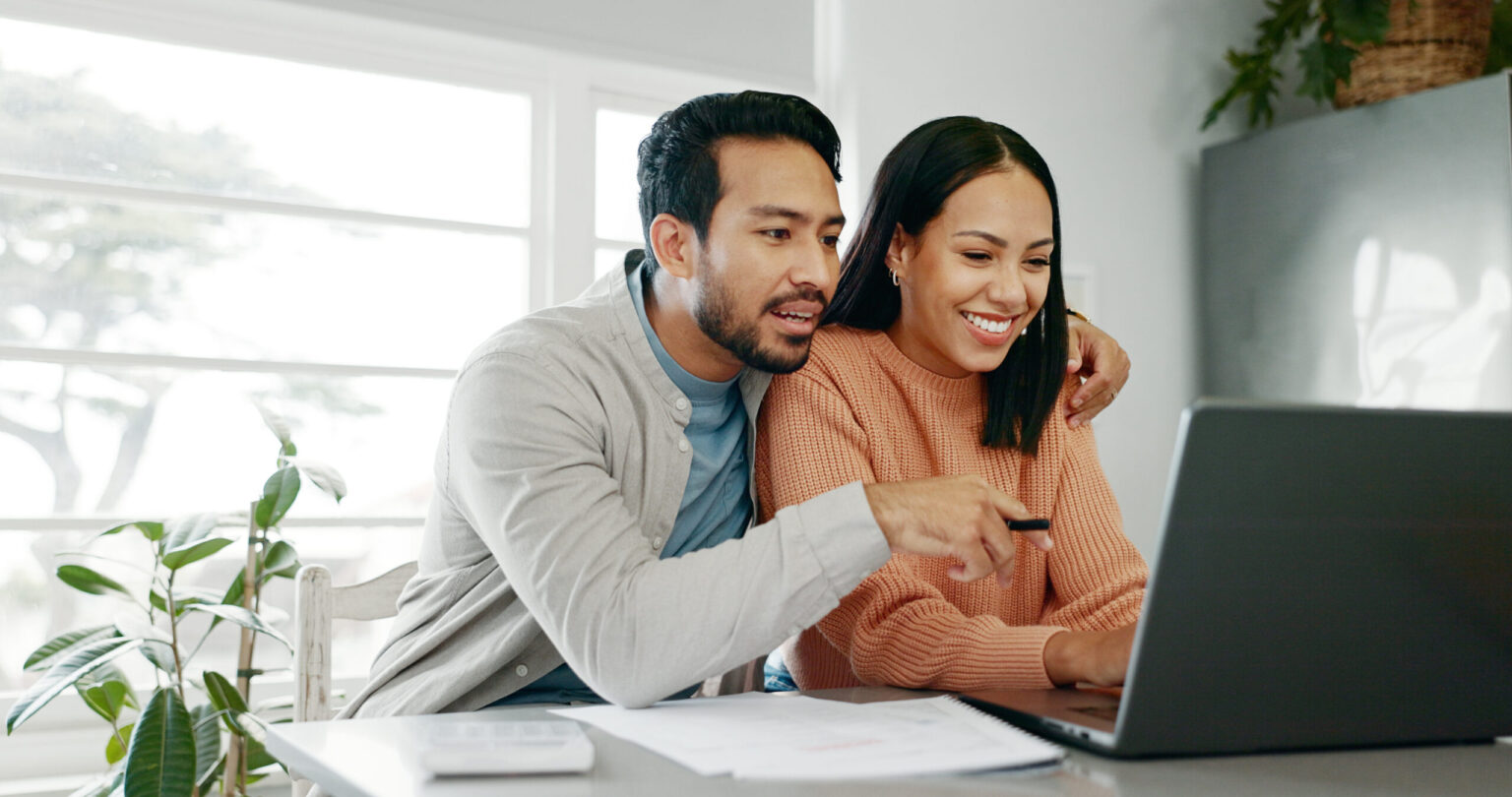 A couple smiling while looking at a laptop