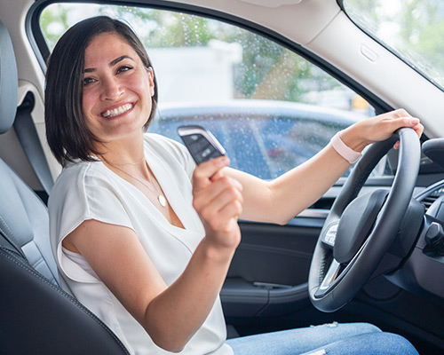 Woman in car holding card and smiling.