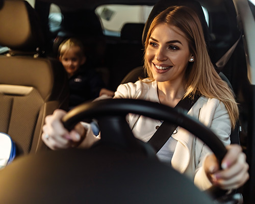 Young mother driving a car with a child in the backseat.