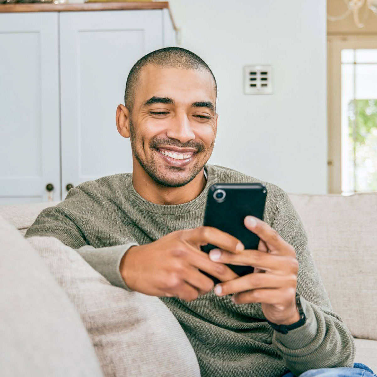 Photograph of a man smiling while using a smartphone.