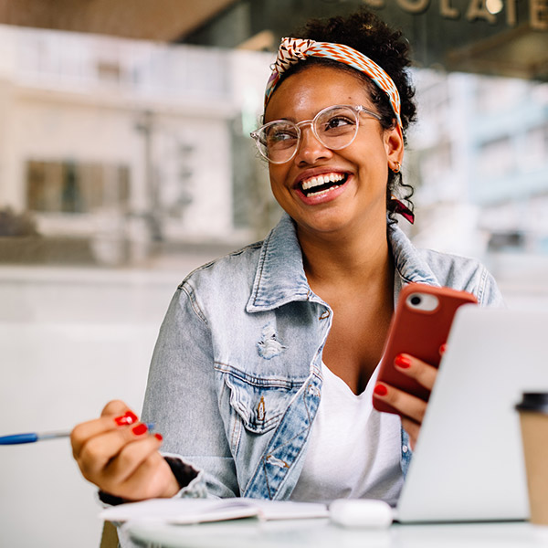Woman smiling and looking at phone and writing stuff down.