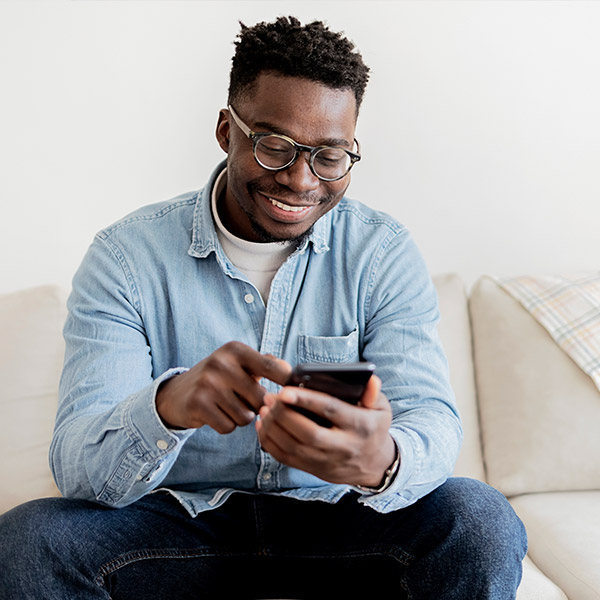 Man sitting on couch while using a smartphone.