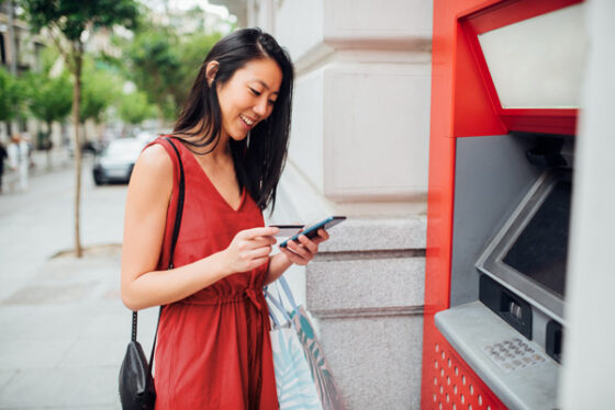 A woman on her phone in front of the atm machine.