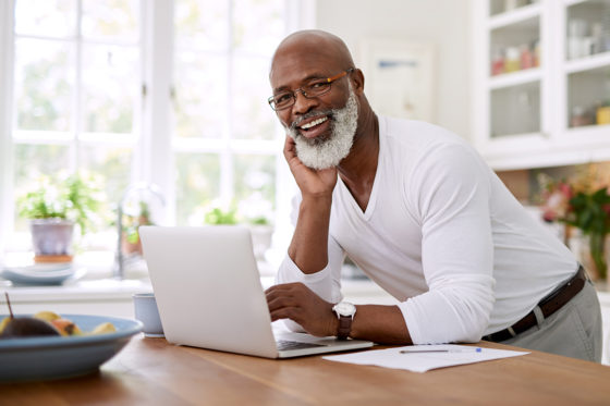 older smiling gentleman using laptop computer on kitchen counter