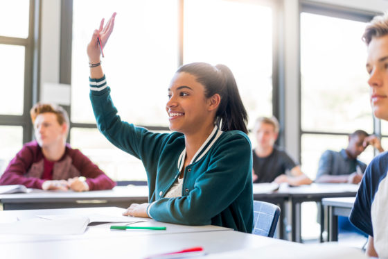 female student at desk with raised hand