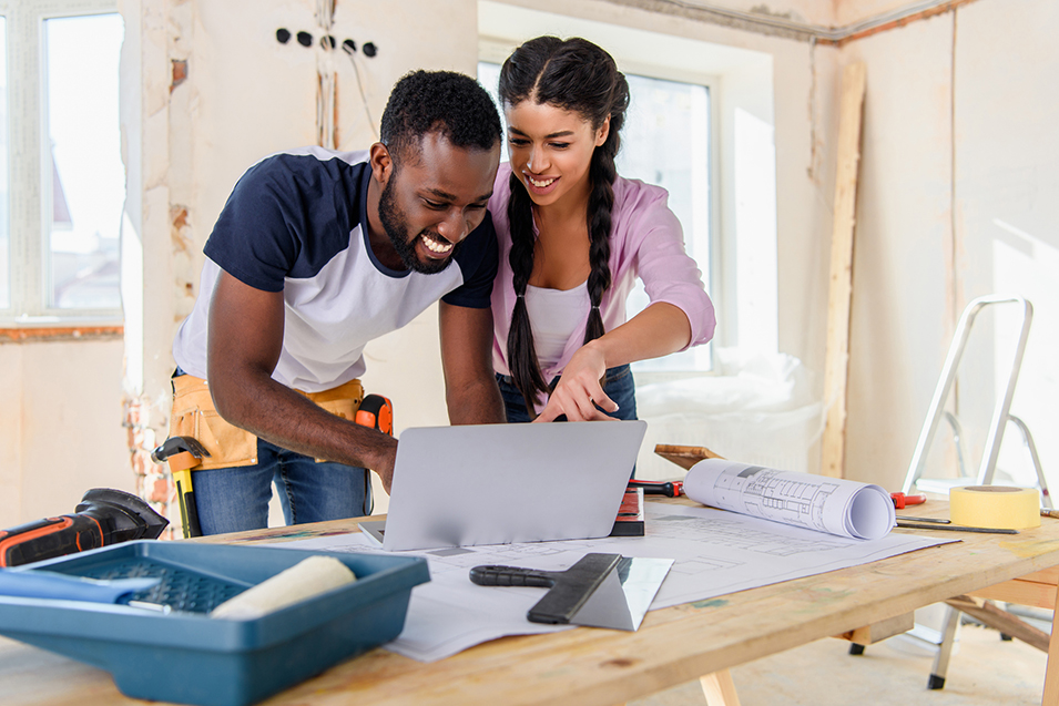 Young African American woman pointing at laptop screen to boyfriend during renovation of home.