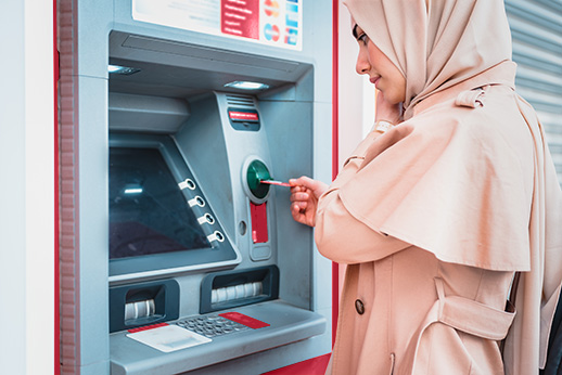 Muslim woman in headscarf and fashionable modern trendy clothes pulls in debit card at an ATM.ATM cash terminal with display