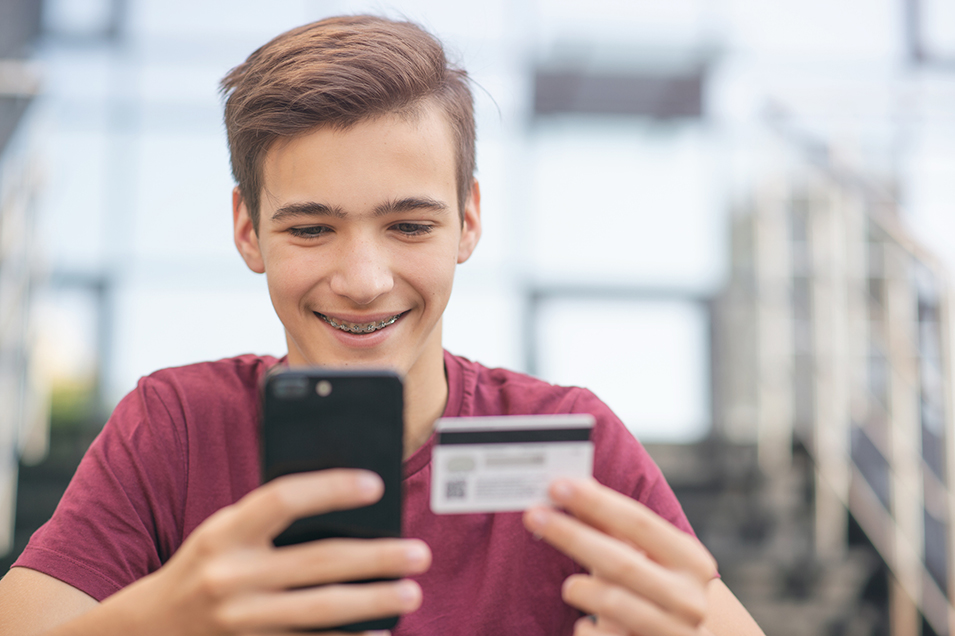 Teenage boy with a credit card and mobile phone makes purchasing outdoors.