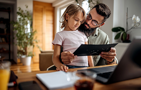 Father working from home while holding his daughter in lap.