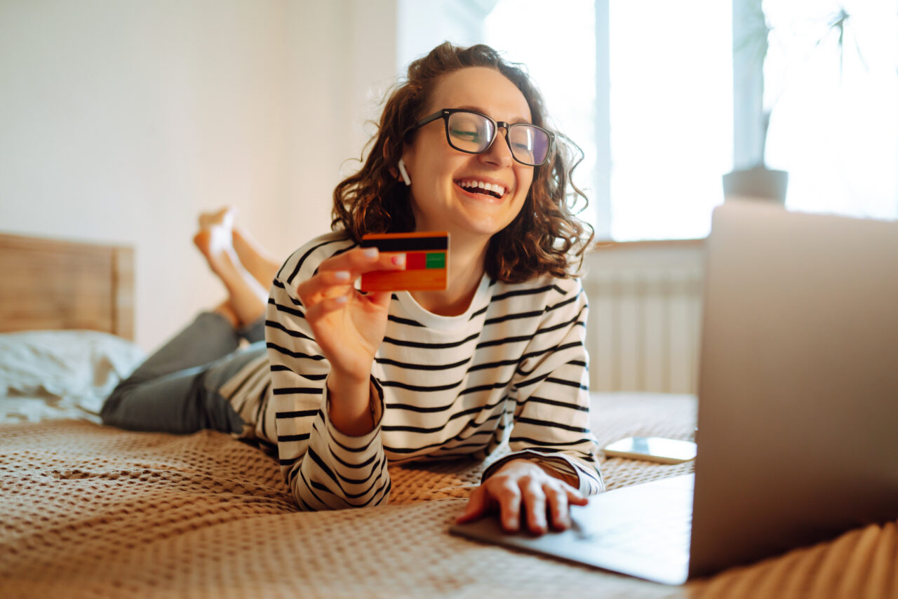 A young woman holds a credit card and uses a laptop.