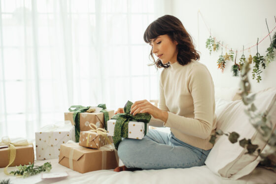 Side view of woman sitting on bed at home packing christmas presents. Woman celebrating christmas sitting at home.