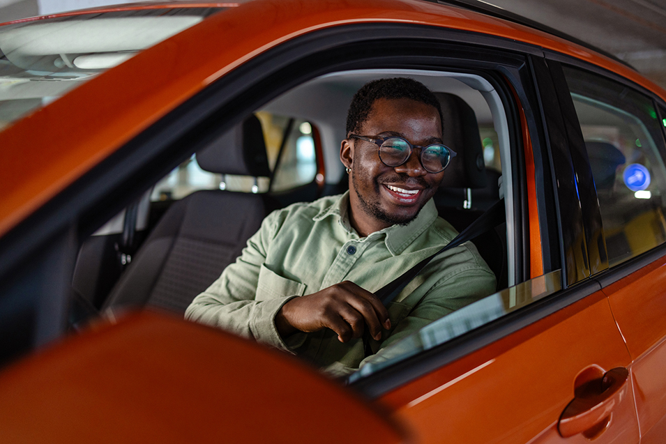 Photo of a male car driver looking through the car window while fastening a safety belt