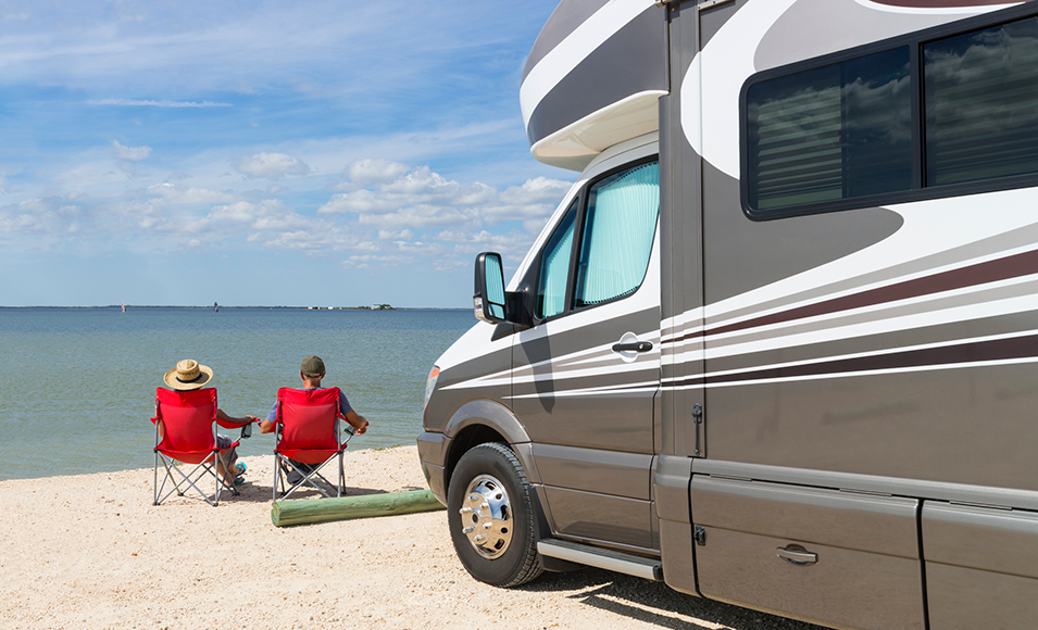 Senior couple sitting near water with motorhome in camping.